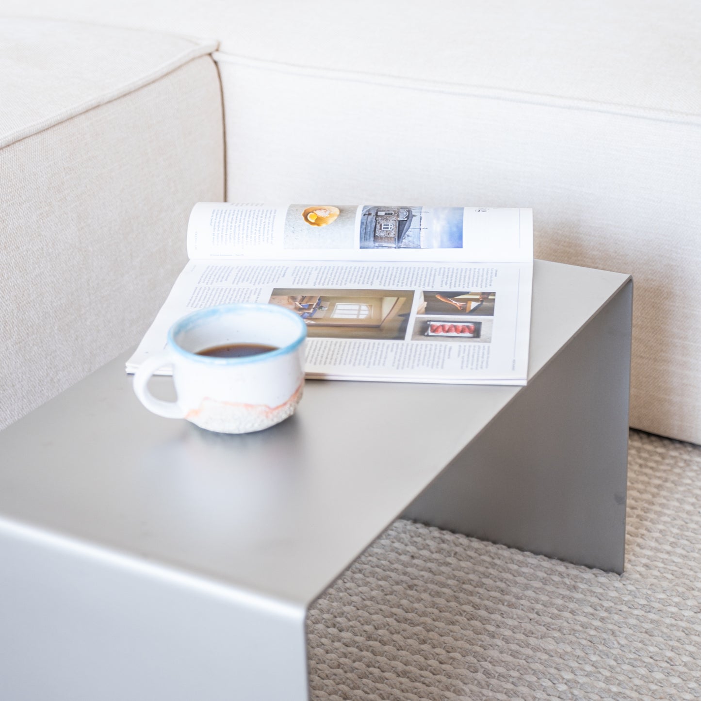 Alternate angled composition of the Elegance Side Table in reversed position with coffee cup and magazines.