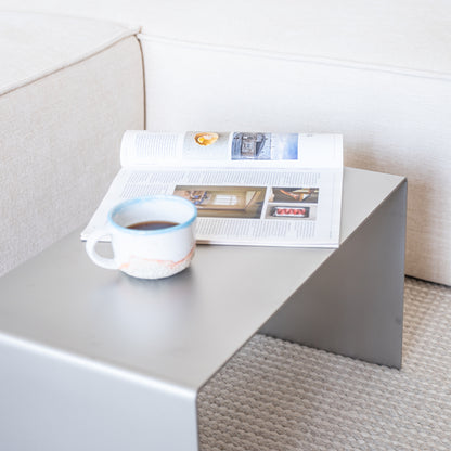 Alternate angled composition of the Elegance Side Table in reversed position with coffee cup and magazines.