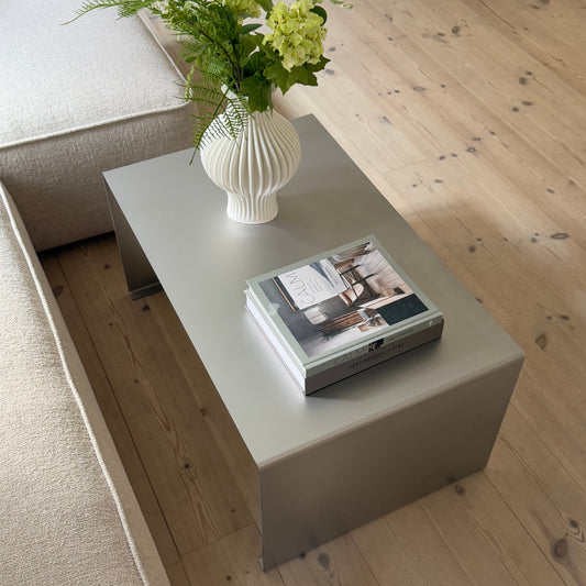 Metal coffee table in satin matte stainless steel styled with books and a white ceramic vase.